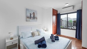 Une chambre à coucher avec un lit, une table de chevet, un tableau représentant un pont et une fenêtre avec des rideaux.