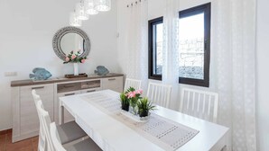 Un coin repas avec une table blanche, des chaises, un miroir décoratif et une fenêtre avec des rideaux.