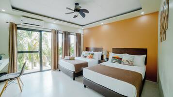 A hotel room with two beds, a ceiling fan, an air conditioning unit, a desk with a chair, and a view of palm trees through the glass door.