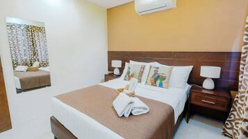 Habitación de hotel con cama, mesita de noche, aire acondicionado de pared y espejo con marco decorativo.