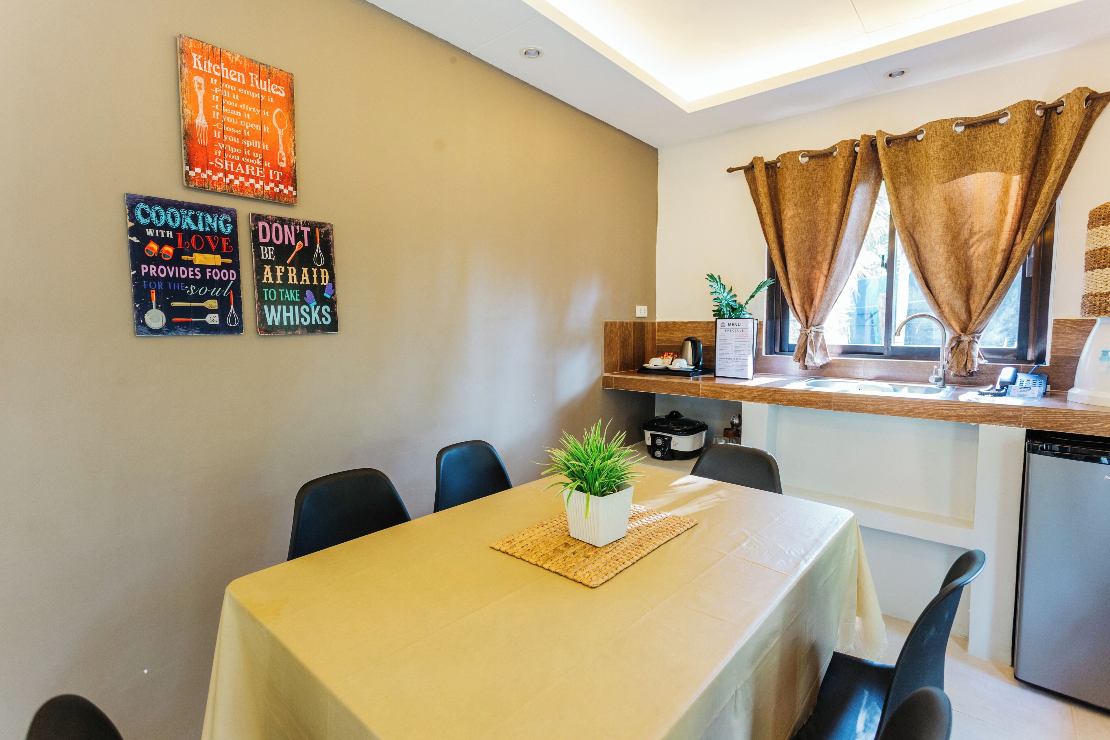 A dining area with a table set for two, a small potted plant, and kitchen utensils on the wall.