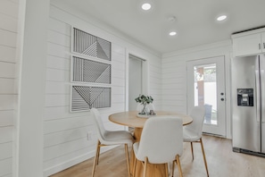 Eine moderne Küche mit weißen Schränken, einem Edelstahl-Kühlschrank, einem runden Holztisch mit zwei weißen Stühlen und Wanddekoration.