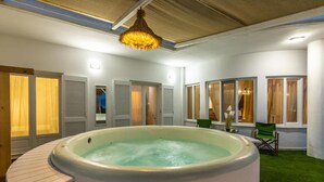 A hot tub in a room with a wooden ceiling, white walls, and a green lawn outside. - White Cycladic House With Jacuzzi (Hersonissos)