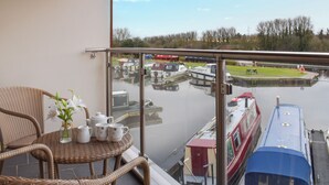 A balcony with wicker furniture, a view of a canal with boats, and a red boat docked at the pier. - 1 bedroom accommodation in Carnforth (Carnforth)