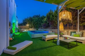 Een goed verlicht terras buiten met een jacuzzi, zitplaatsen en een pergola.