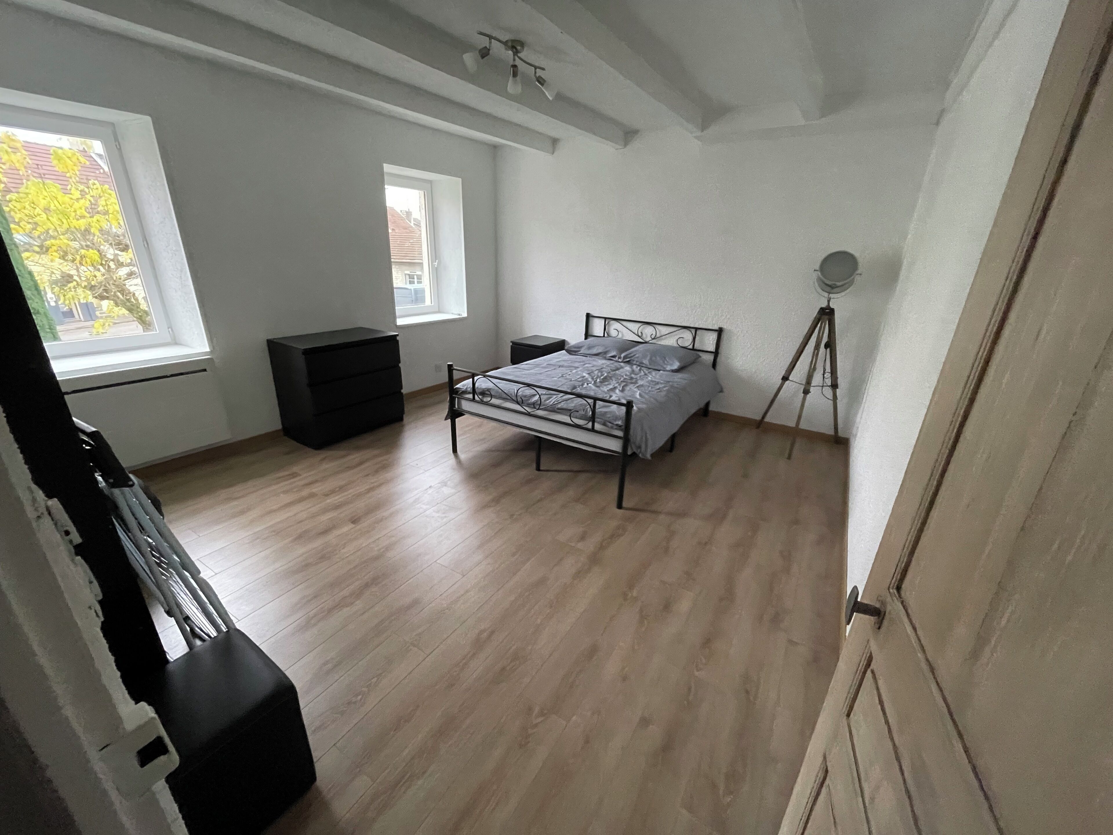 A bedroom with a bed, a dresser, a window, and a tripod lamp.
