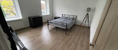 Ein Schlafzimmer mit einem Bett, einem Schminktisch, einem Fenster und einer Stehlampe.