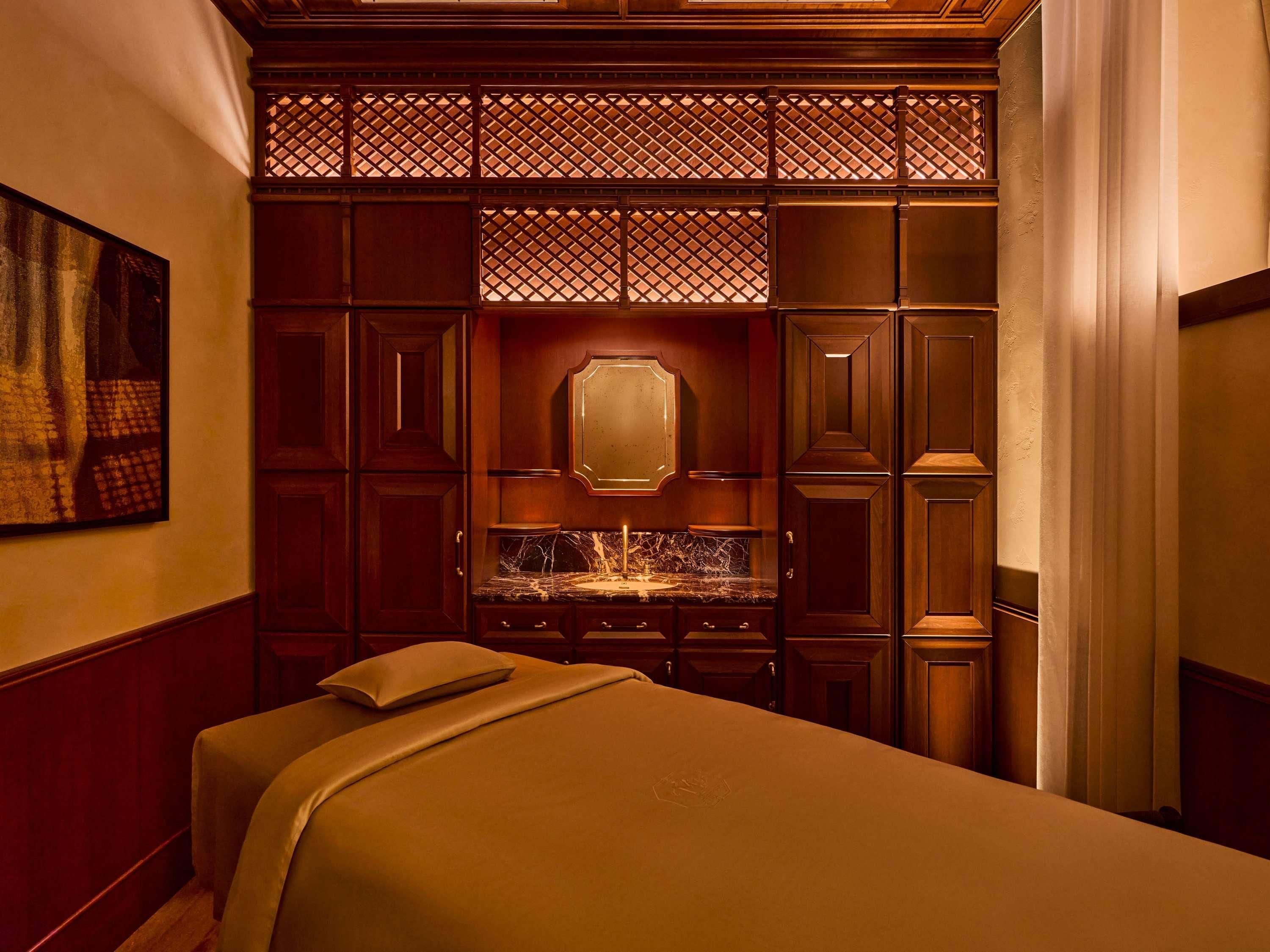 A hotel room with a bed, a mirror, a sink, and a wooden partition.