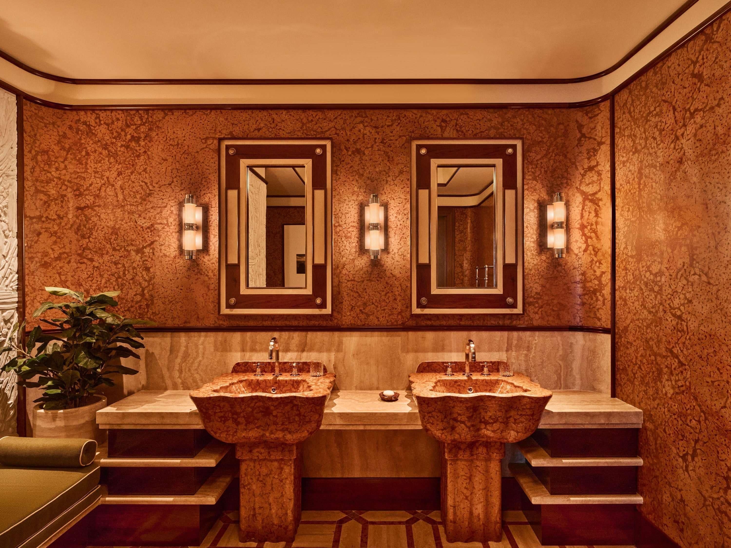 A bathroom with two sinks, wall-mounted mirrors, and sconces.
