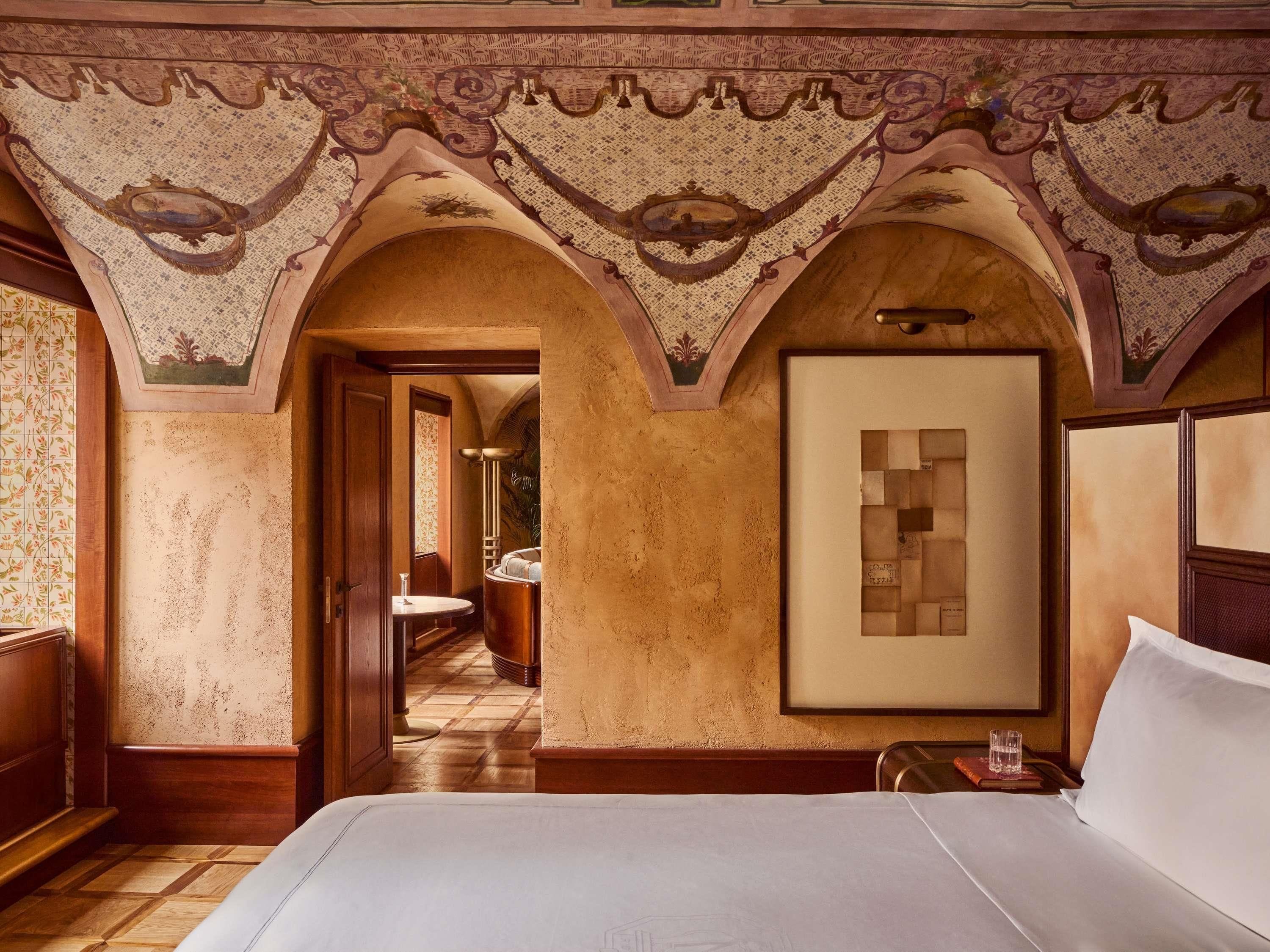 Quarto de hotel com uma cama grande, uma obra de arte emoldurada na parede e uma porta em arco que dá para um banheiro.