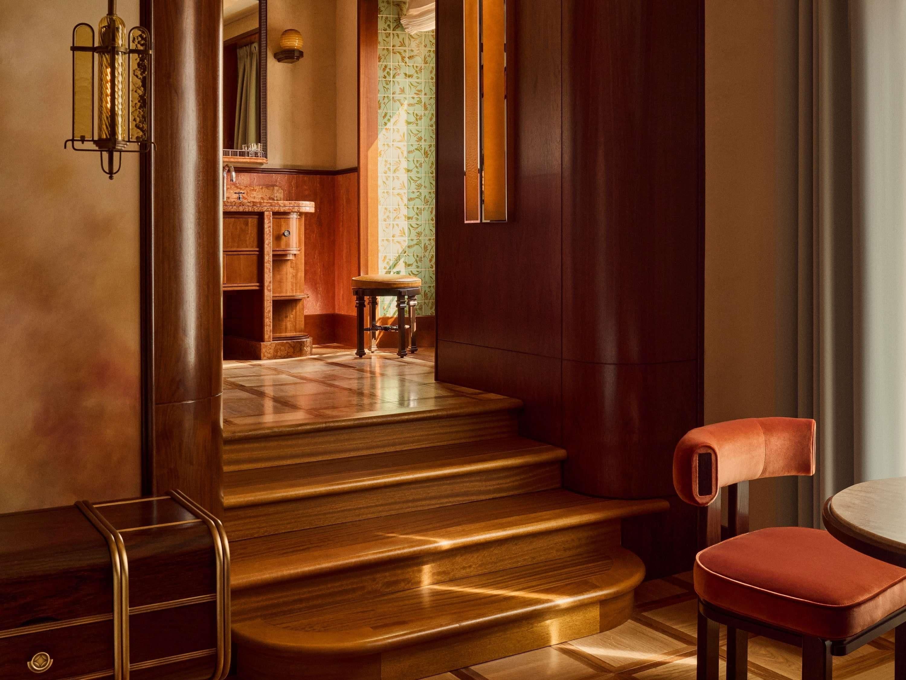 A hotel lobby with a wooden staircase, a round table, and a leather chair.