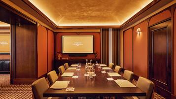 A conference room with a long table, chairs, a projector screen, and a carpeted floor.