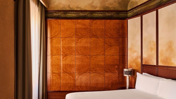 A hotel room with a large bed, a wooden wardrobe, and a nightstand with a lamp.
