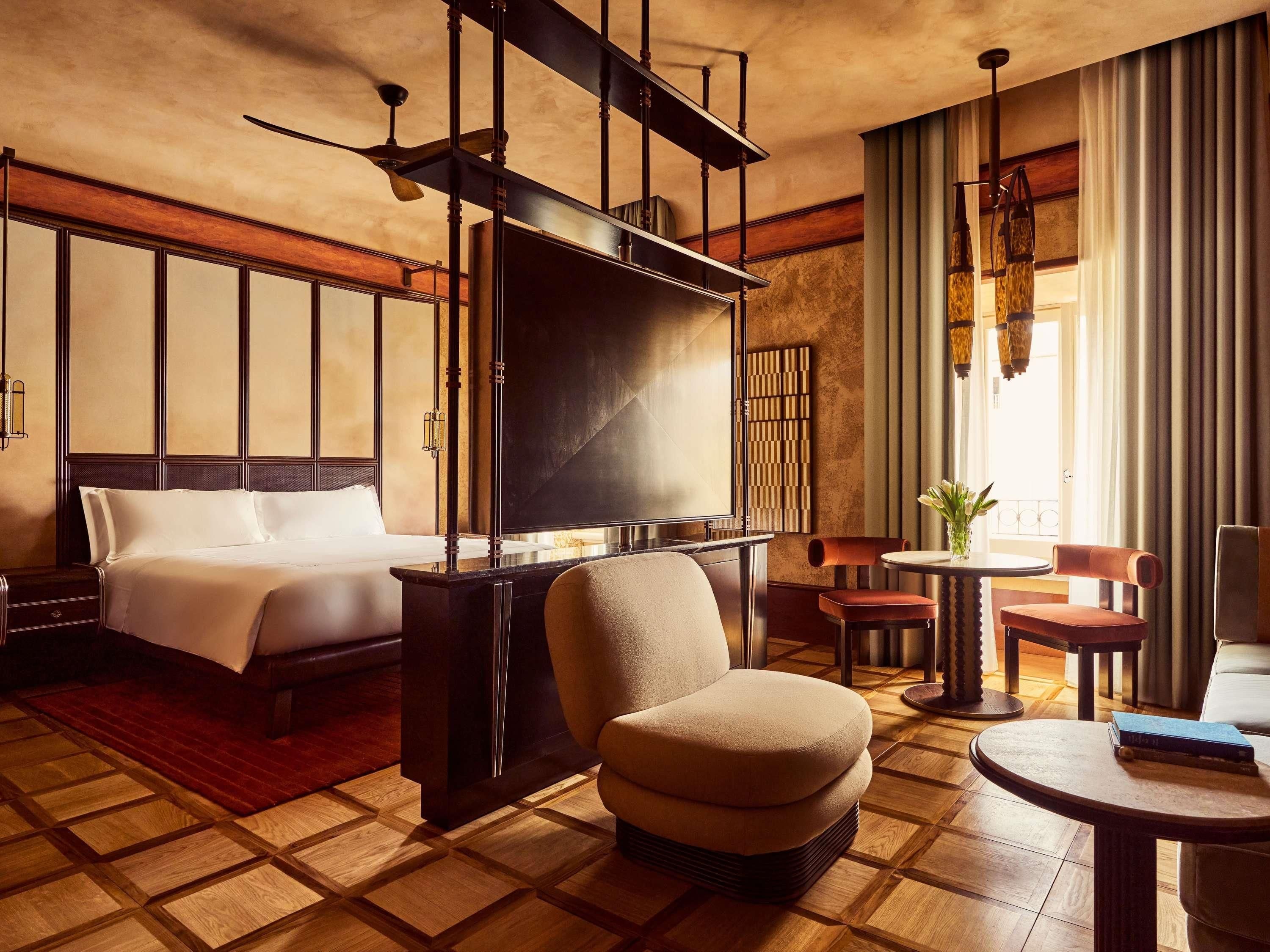 A hotel room with a bed, a seating area with a table and chairs, a television, and a large window with curtains.