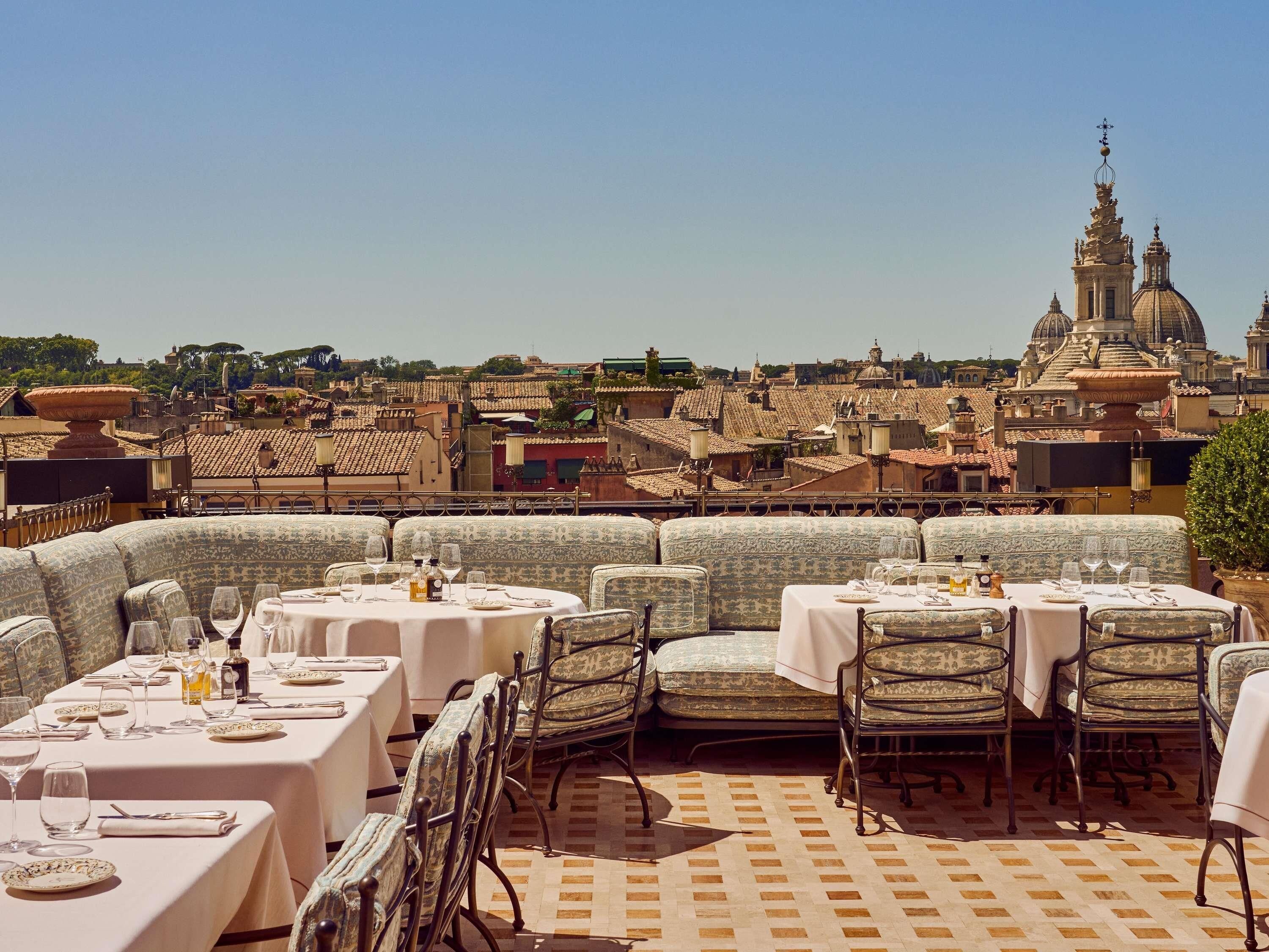 Un espacio para comer al aire libre con mesas y sillas, con vistas a un paisaje urbano con edificios históricos.