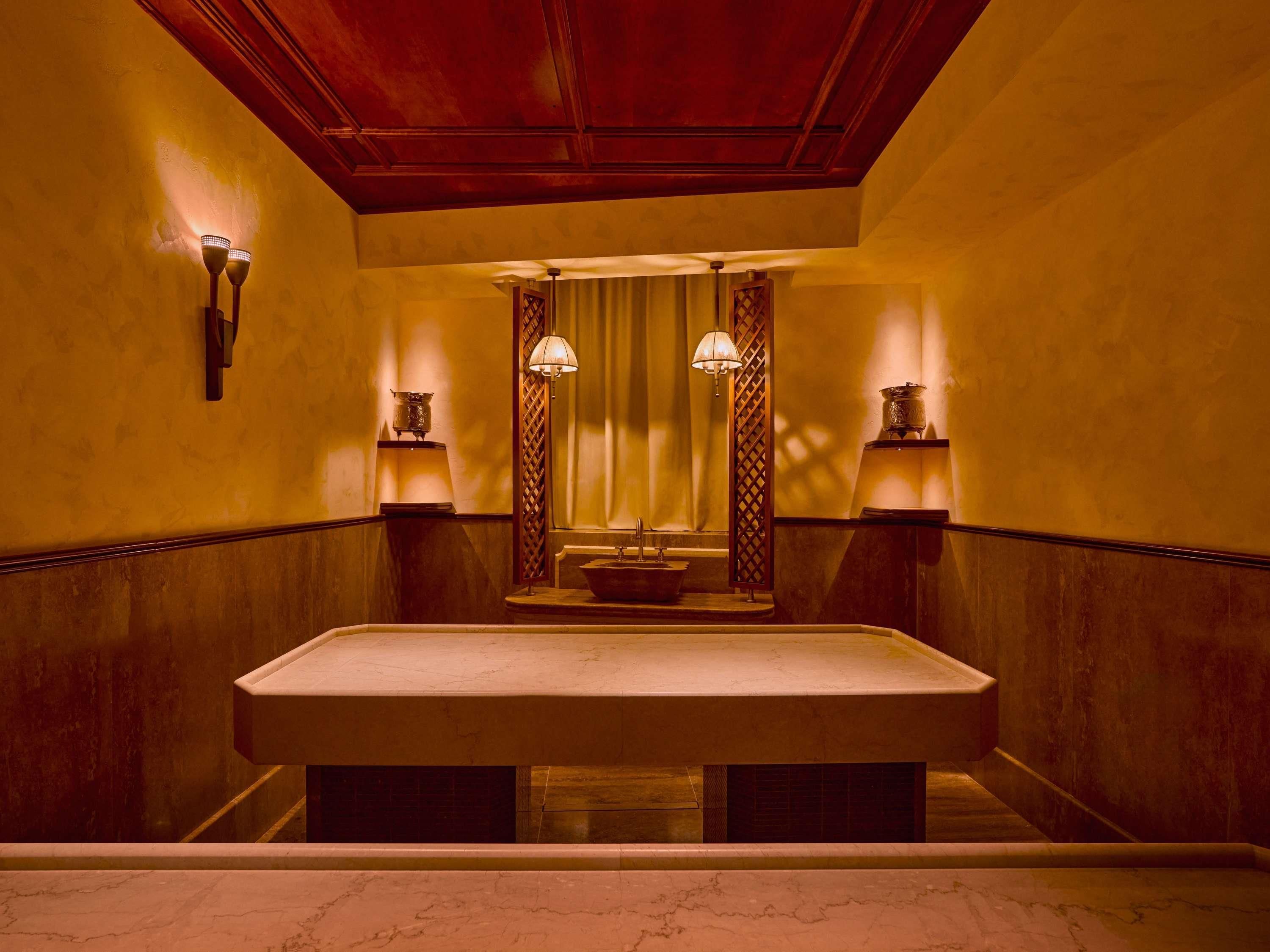 A bathroom with a large marble sink, two wall-mounted lamps, and a mirror above the sink.