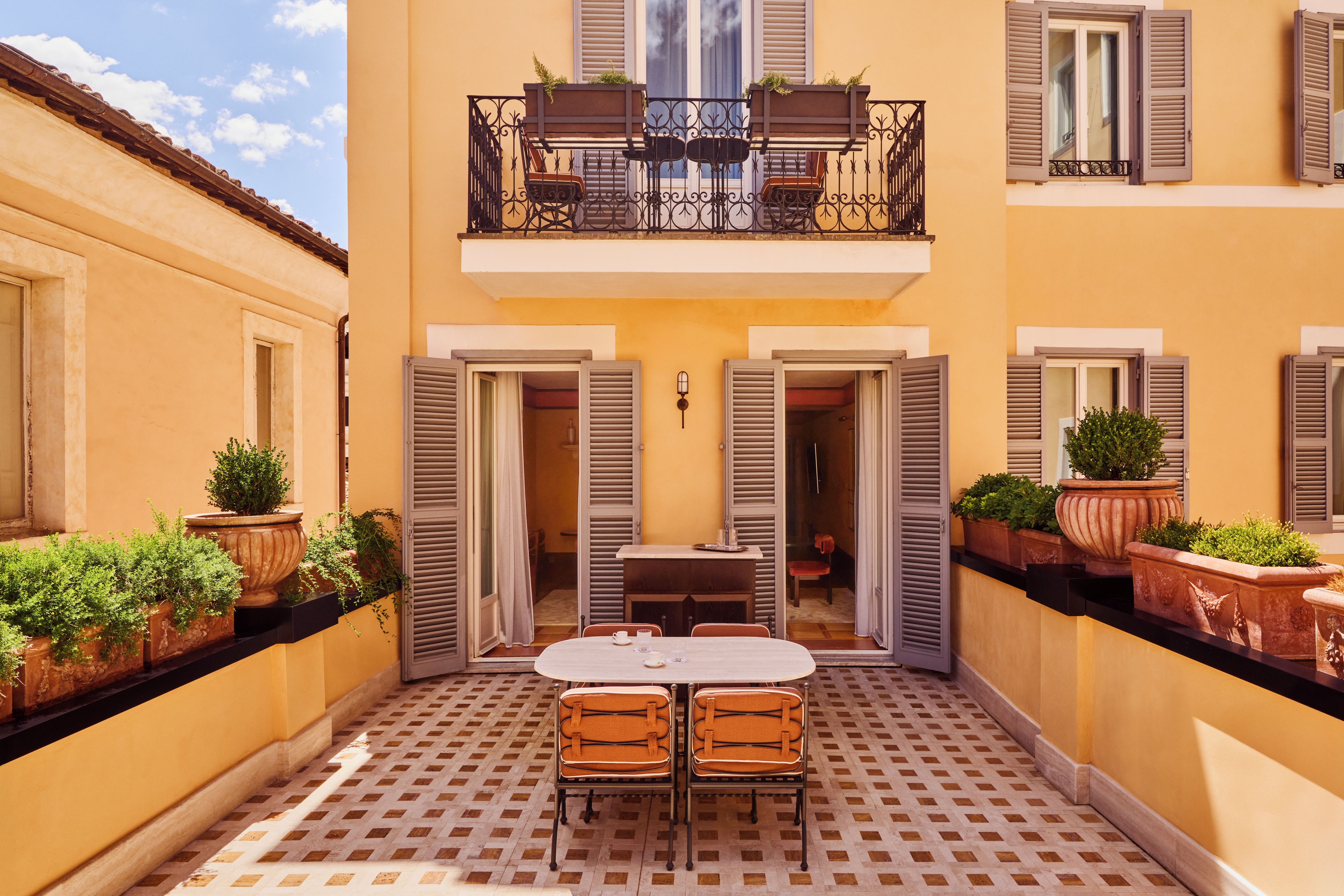 Une cour avec une table et des chaises, des plantes en pot et un balcon doté d’une balustrade.