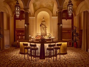 A bar area with a central statue, bar stools, and a patterned floor. - Orient Express La Minerva (Rome)