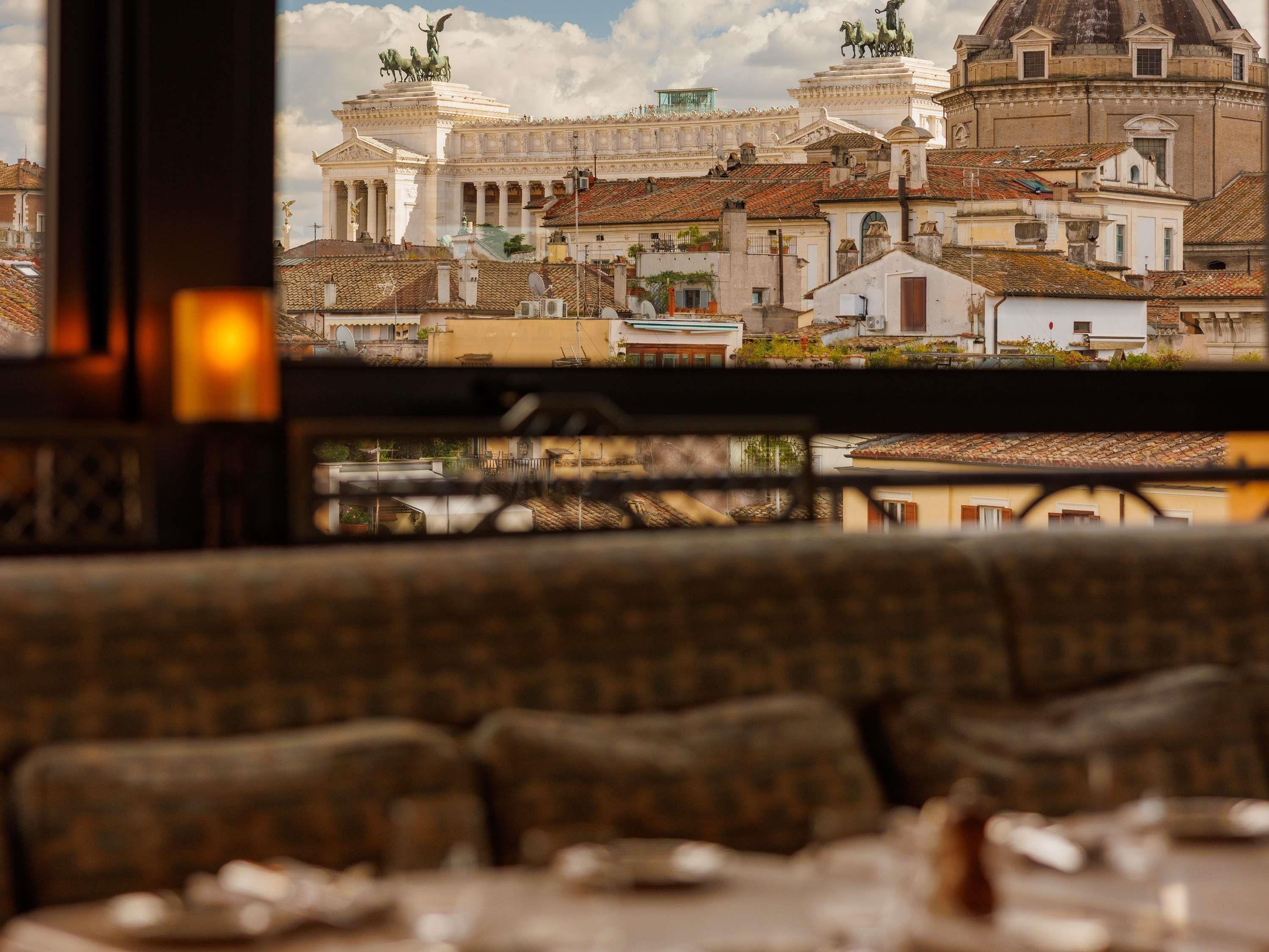 A view of a historic building with classical architecture, including domes and statues, from a window overlooking a dining area with a sofa and table set.