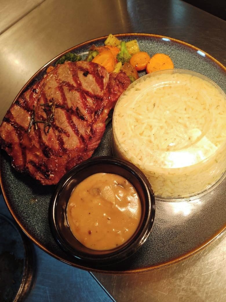 A plate with grilled steak, vegetables, mashed potatoes, and a side of gravy.
