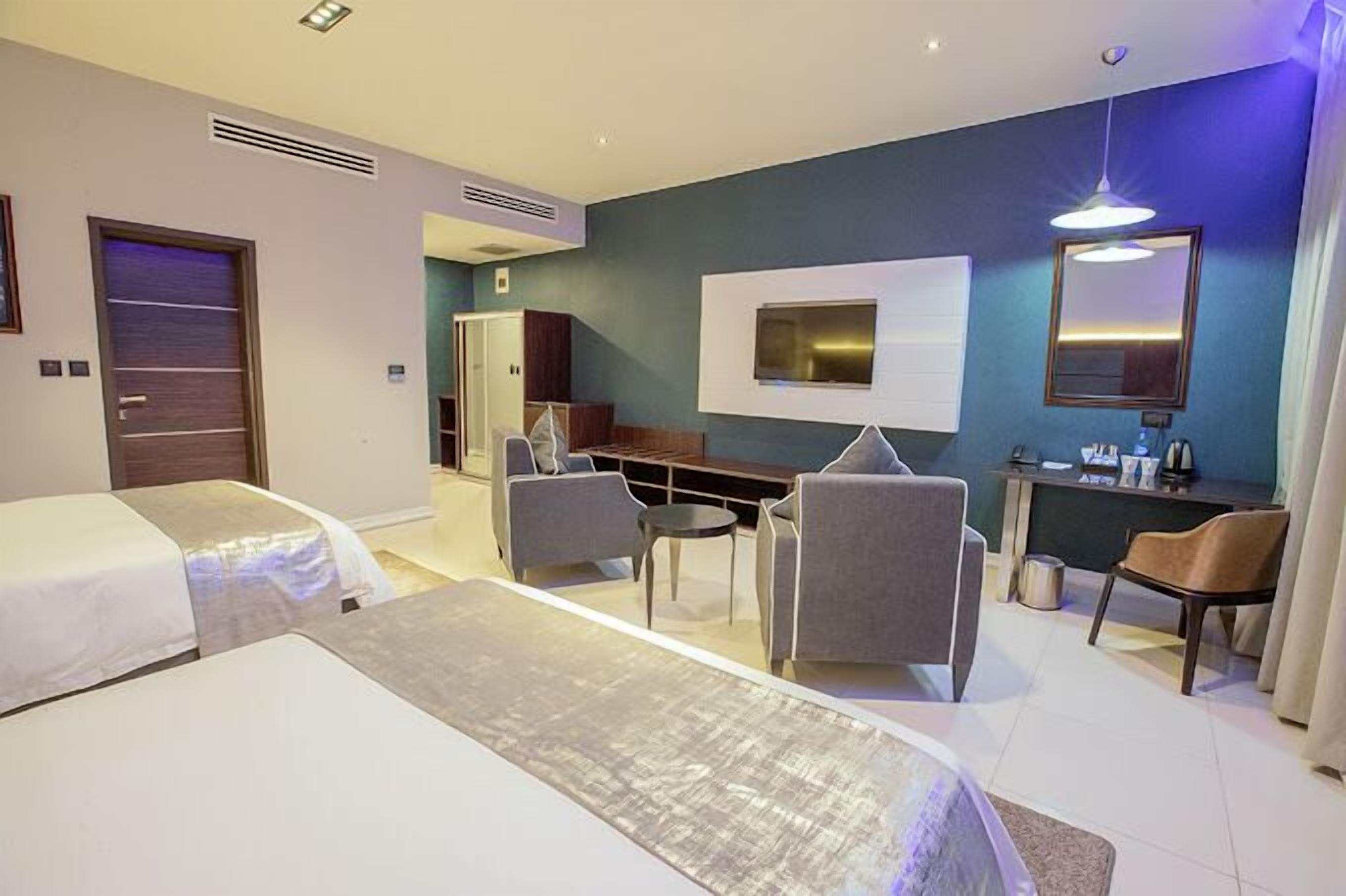 A hotel room with two beds, a seating area with chairs, a TV, and a desk with a mirror.