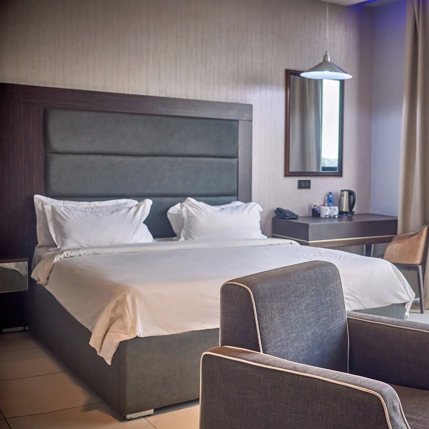 A hotel room with a large bed, a chair, a desk, and a mirror.