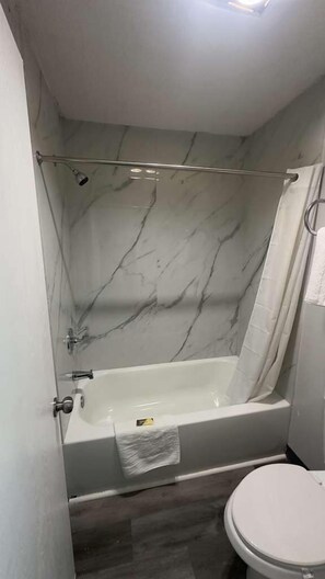 A bathroom with a marble wall, a bathtub, a shower curtain, and a toilet.