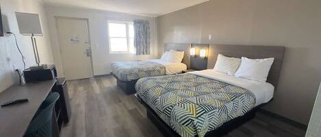 Habitación de hotel con dos camas, un escritorio, una silla, una lámpara y una ventana.