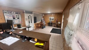 Une pièce avec un bureau en bois, un ordinateur et des papiers. On y trouve également une table à manger avec des chaises et une cheminée.