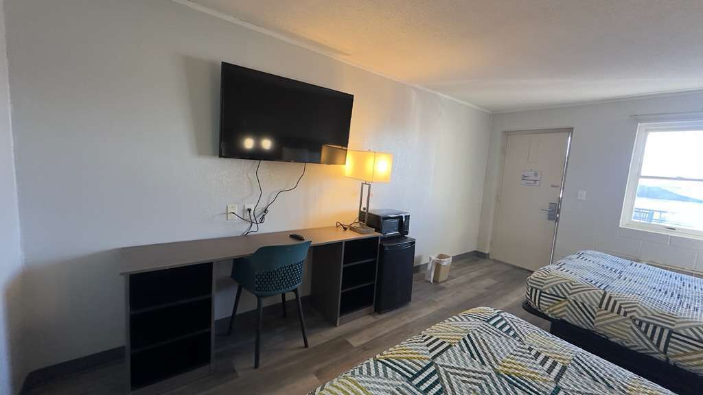 Een kamer met een bureau, stoel, twee bedden, een televisie en een raam.