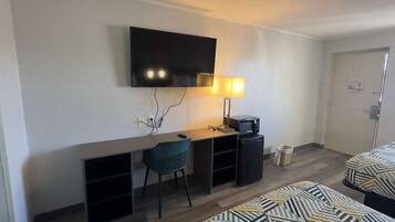 A hotel room with a desk, chair, television, and two beds.