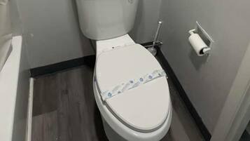 Ein kleines Badezimmer mit Toilette, Handtuchhalter mit zwei Handtüchern und Toilettenpapierhalter.