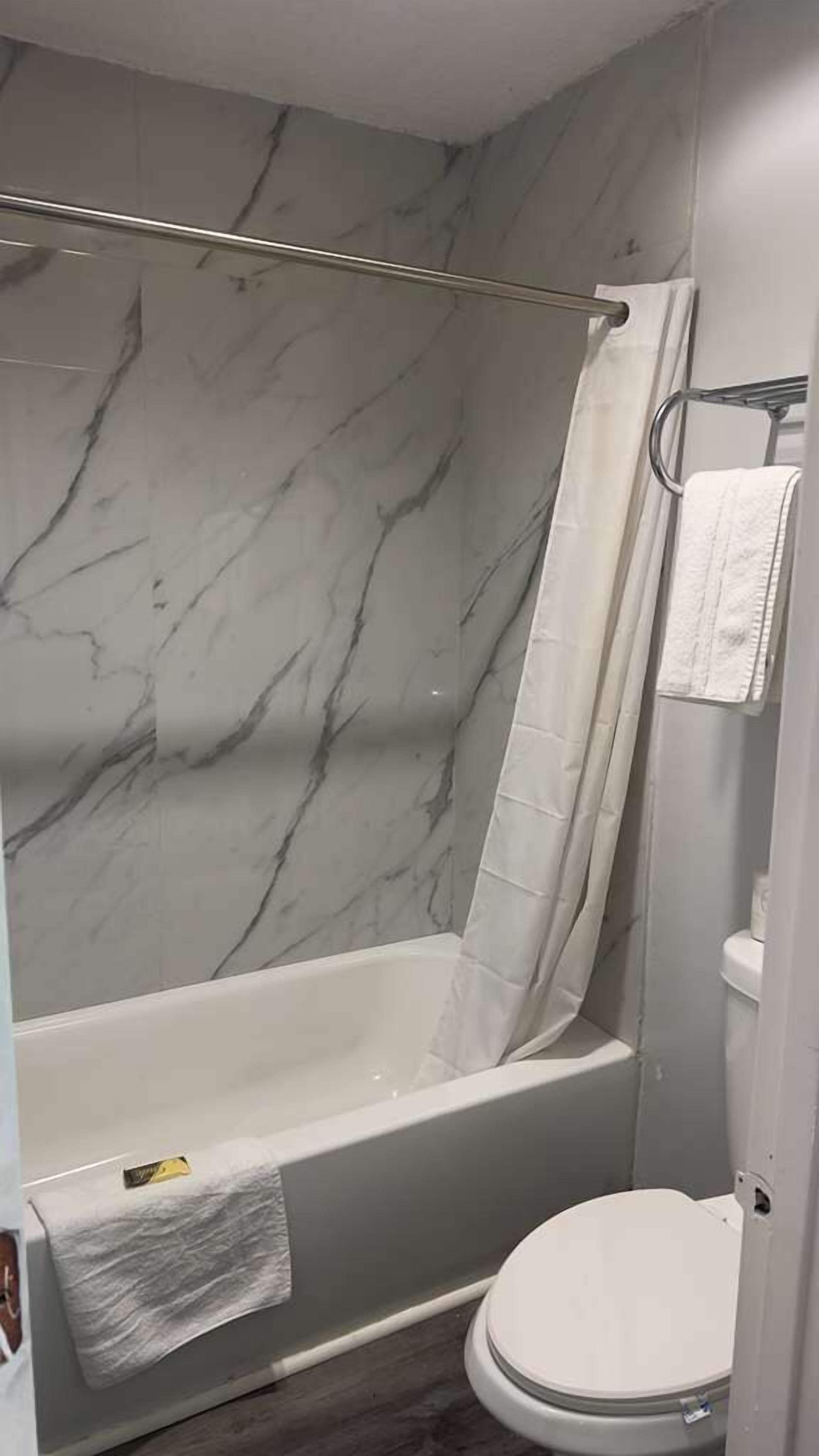 Un bagno con parete in marmo, una vasca, un water e un porta asciugamani.
