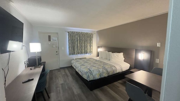 A hotel room with a bed, desk, chair, and a TV mounted on the wall.