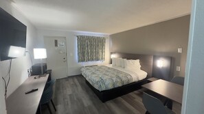 A hotel room with a bed, bedside table, desk, chair, and a television.
