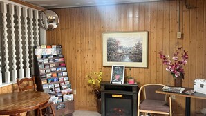 Une pièce chaleureuse avec des boiseries, une cheminée, une bibliothèque et un tableau représentant un paysage, encadré.