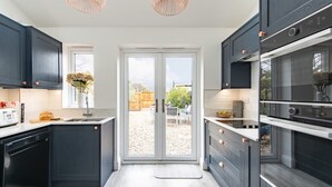 Eine moderne Küche mit dunklen Schränken, einem Geschirrspüler, einem eingebauten Backofen und einem großen Fenster zum Garten.