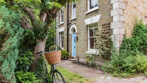 Een fiets met een mandje geparkeerd voor een huis van baksteen met een blauwe deur.