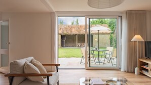 Een moderne woonkamer met een bank, een salontafel en een tv-meubel. Er is een glazen schuifdeur die leidt naar een terras met een tafel en stoelen.