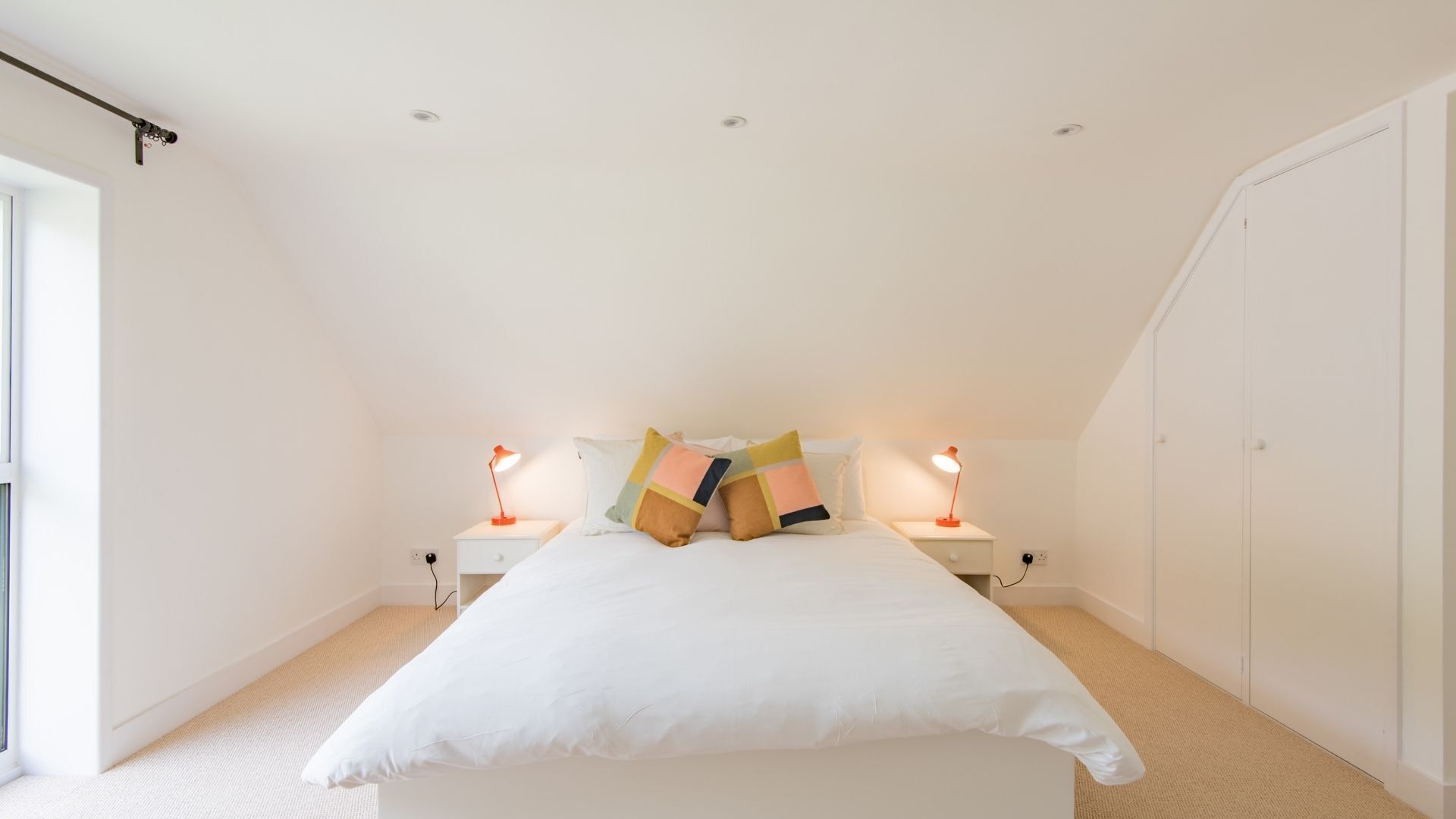Ein Schlafzimmer mit einem großen Bett, zwei Nachttischen mit Lampen, einem Fenster und einer Tür.