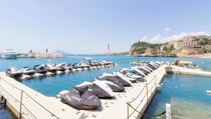 A marina with numerous jet skis docked at the pier, a large yacht, and a clear view of the coastline with buildings and greenery. - - BayAltea (Altea)