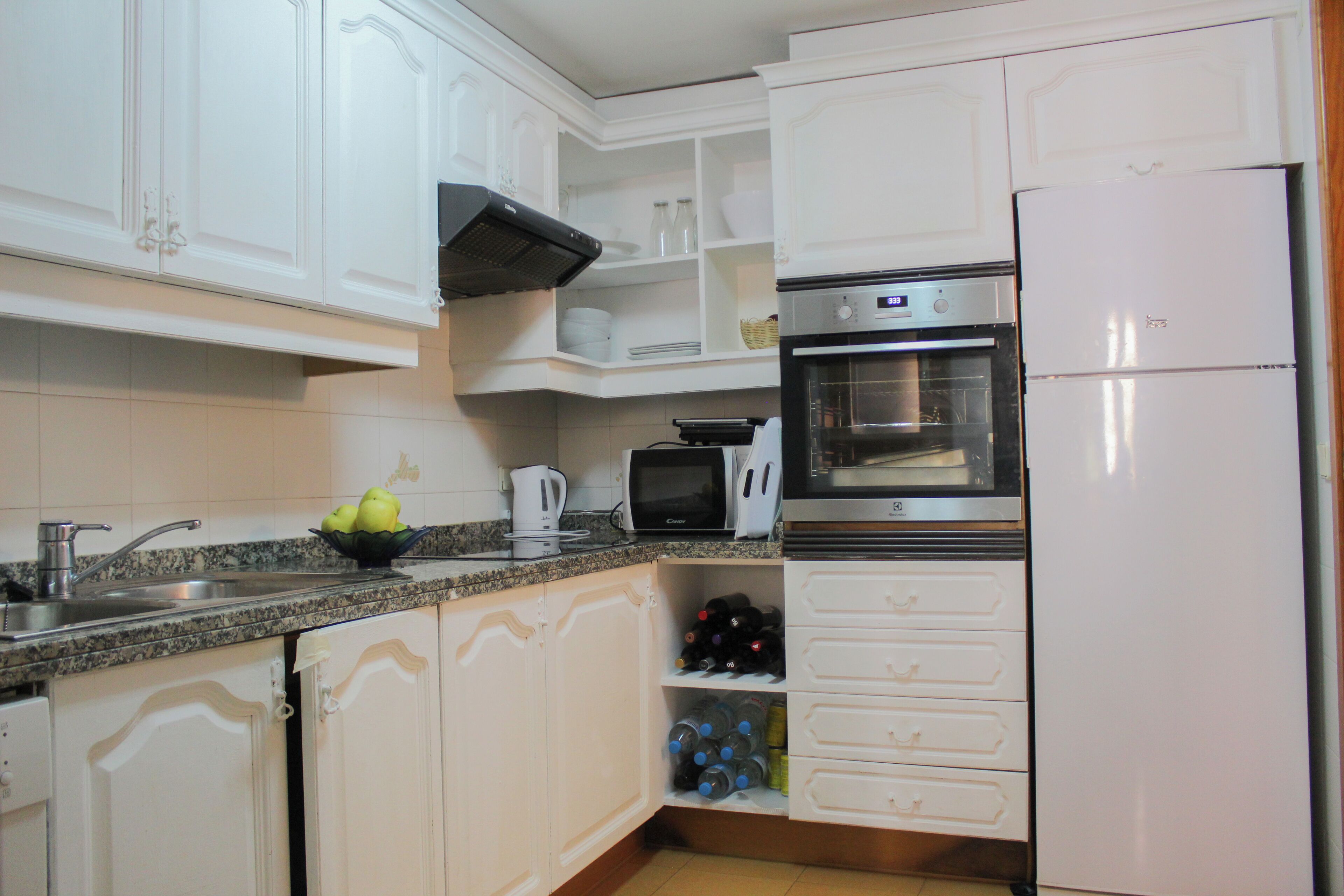 A kitchen with white cabinets, a microwave, an oven, a sink, and a refrigerator.