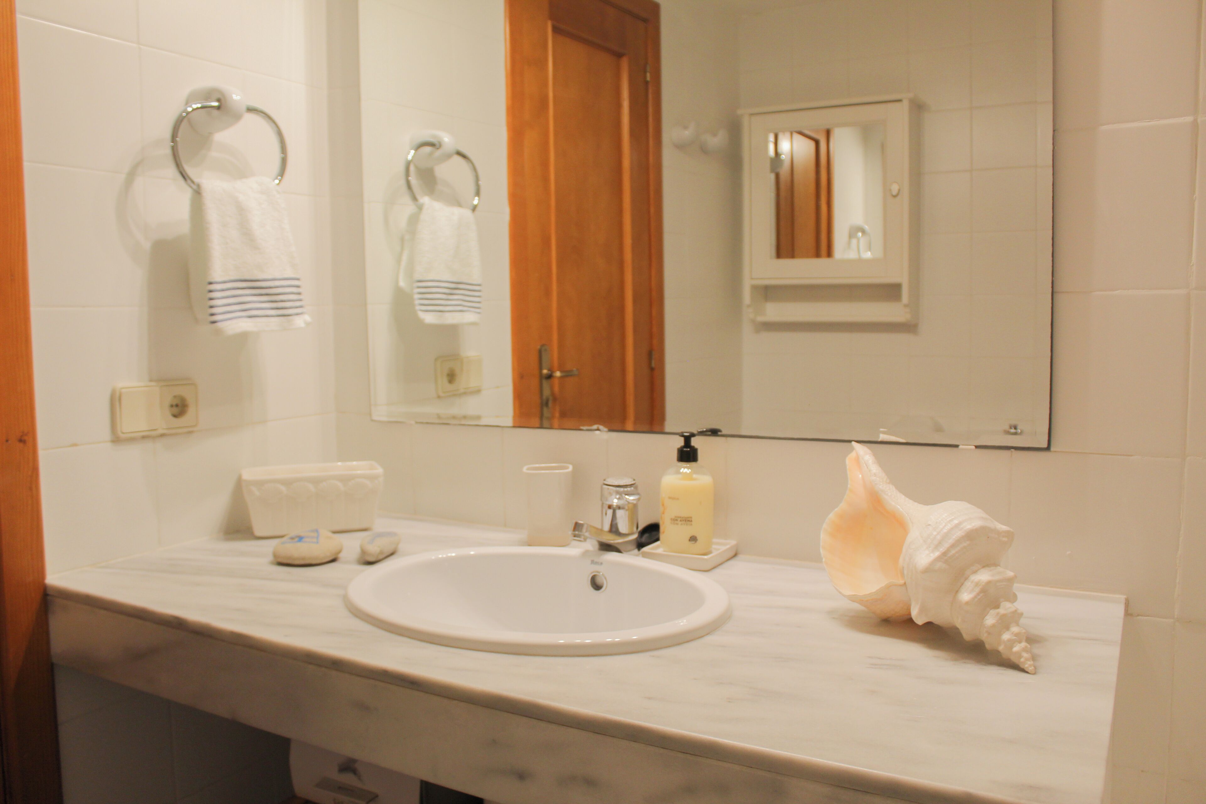 Une salle de bain avec un lavabo blanc, un miroir et une porte en bois.