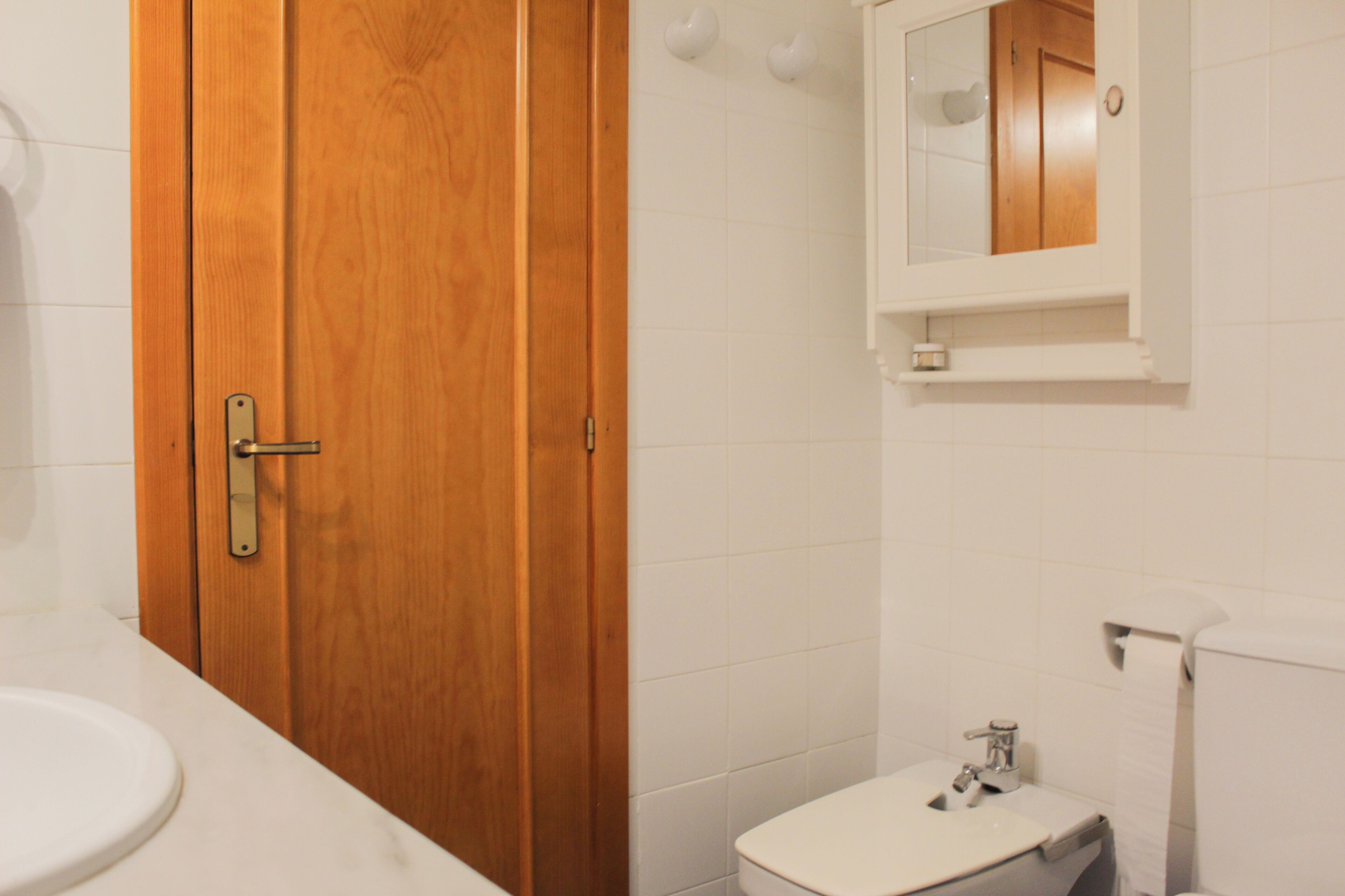 Une salle de bain avec une porte en bois, un lavabo blanc, des toilettes et un miroir au-dessus du lavabo.