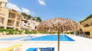 A swimming pool with lounge chairs and a thatched umbrella, surrounded by buildings with balconies and greenery. - - BayAltea (Altea)