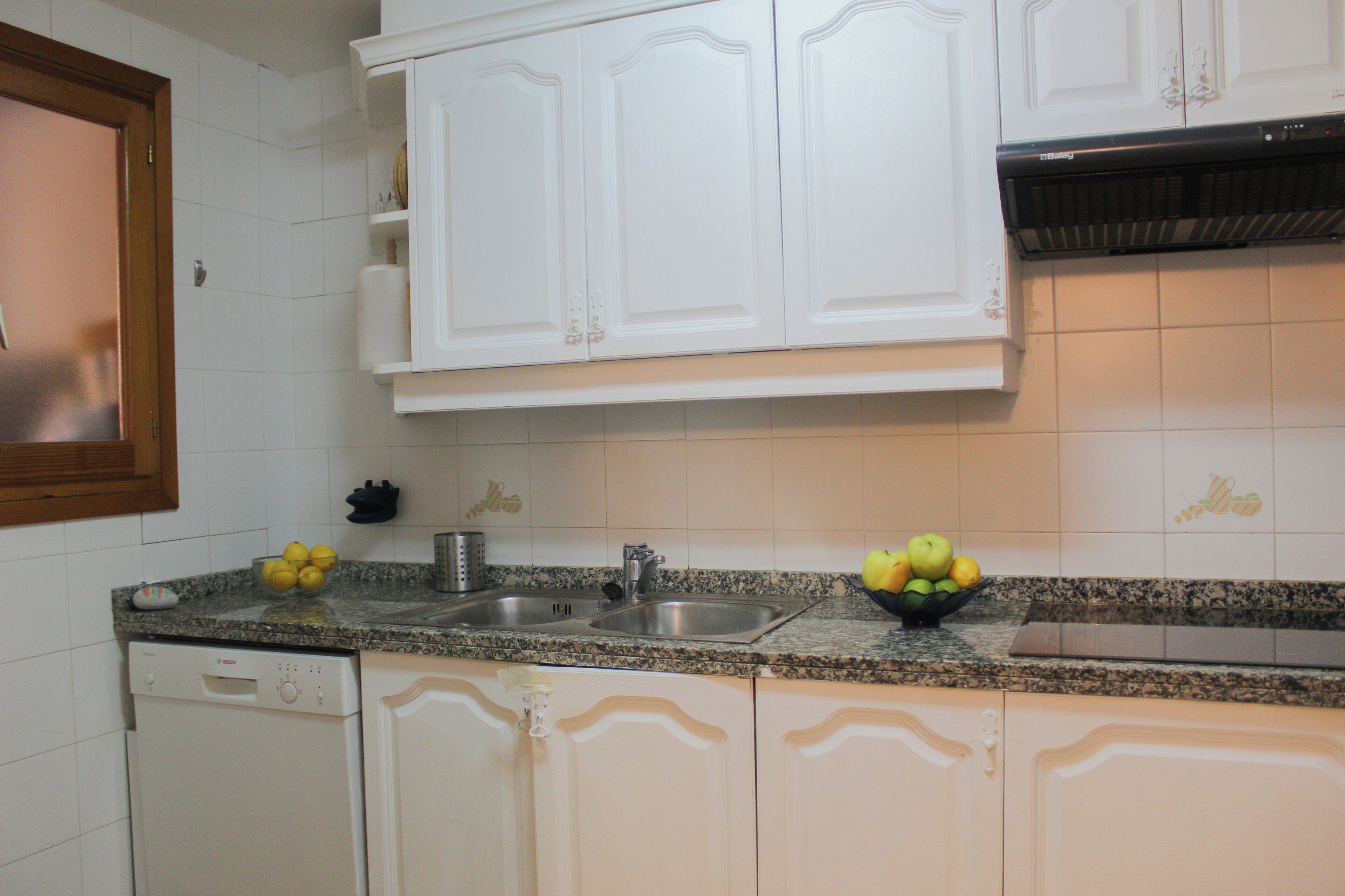 Una cocina con armarios blancos, encimera de granito, lavavajillas y fregadero.