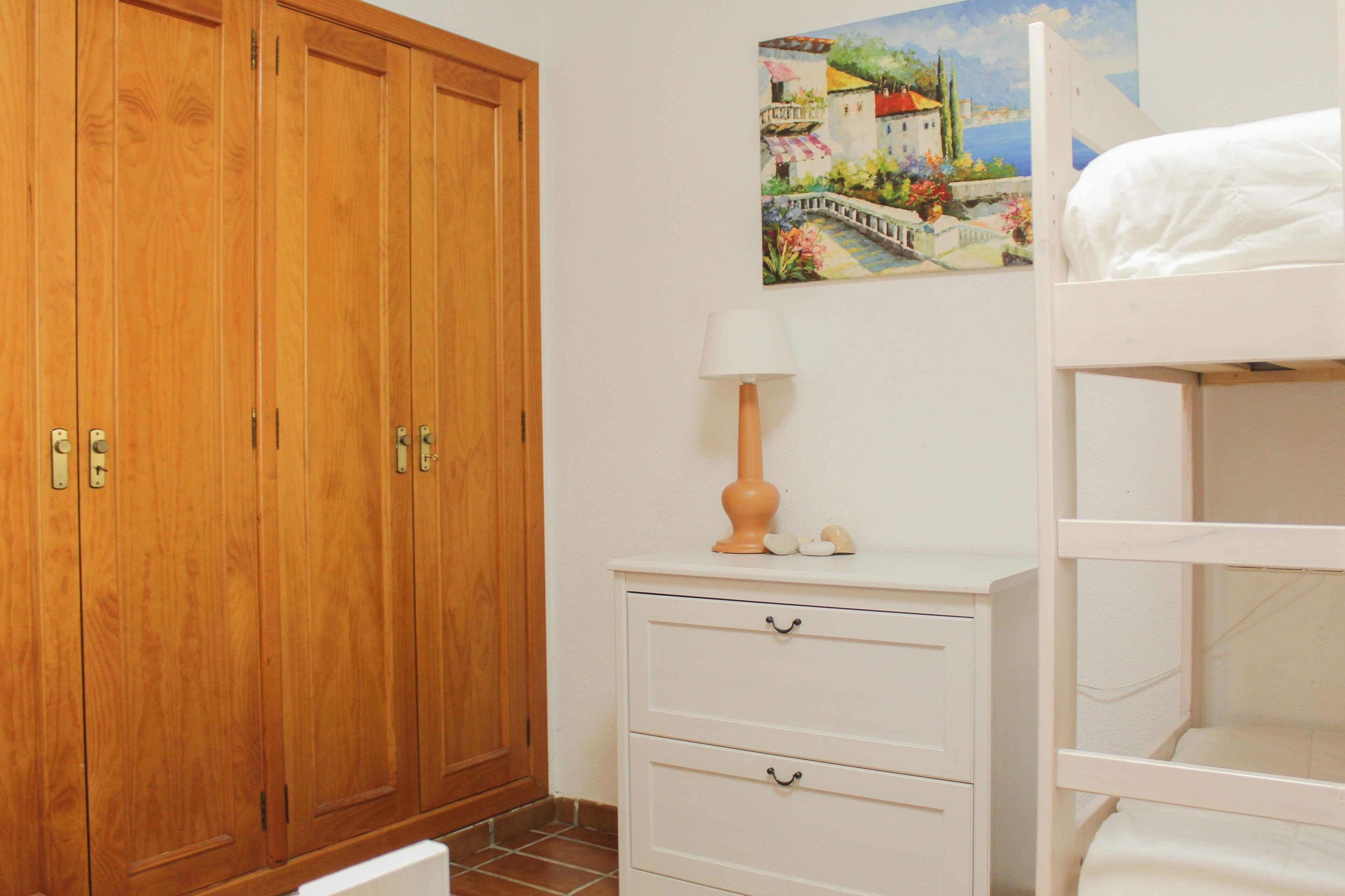 Une chambre avec une armoire en bois, une table de chevet avec une lampe et un lit superposé.