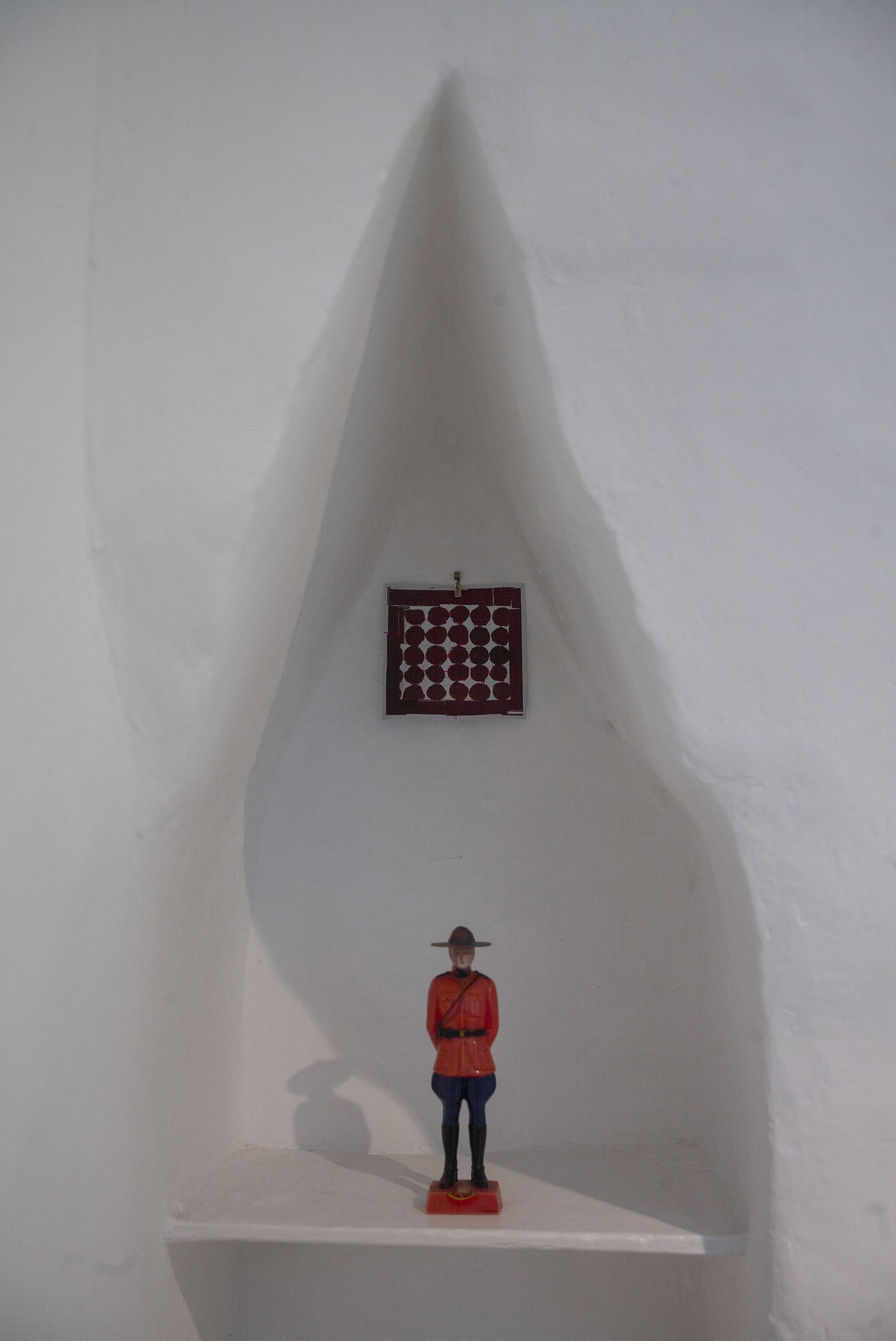A white room with a small shelf holding a figurine and a window with a grid pattern.