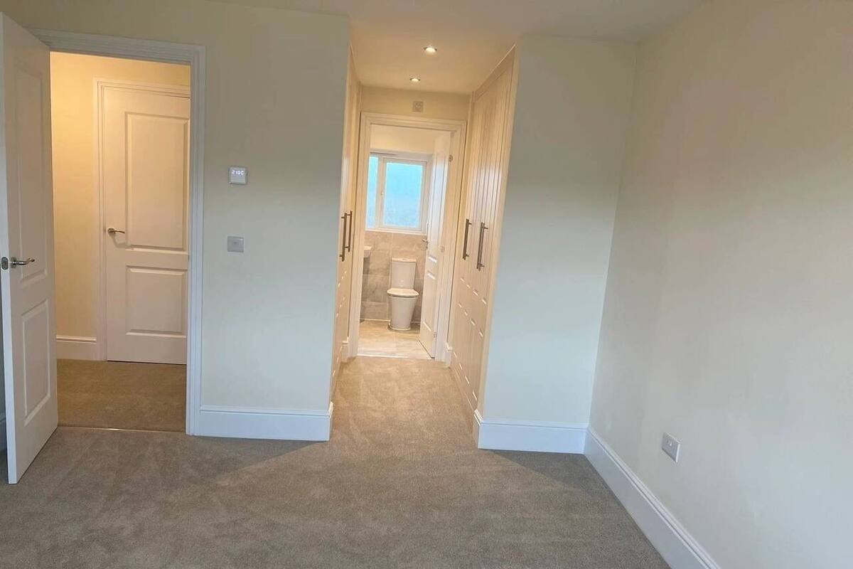 A hallway with carpeted floors, white walls, and a door leading to a bathroom.