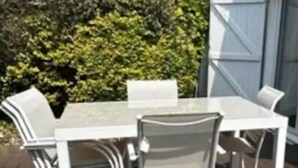 A patio with a white table and chairs, a wooden deck, and a house with a garage door.